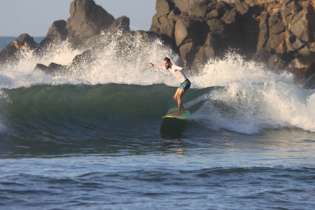 Longboard surfer riding a clean El Salvador wave with rocks behind